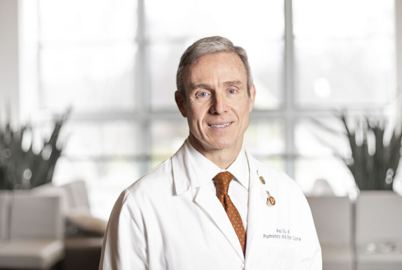 A portrait of Dr. Wes Ely in a white coat in his office.