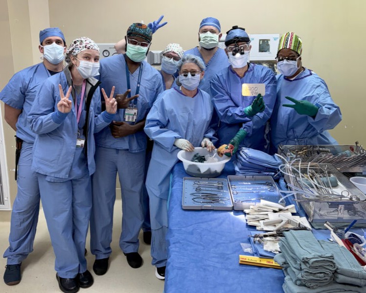 A group of doctors in blue scrubs poses for a phot in a transplant operating room