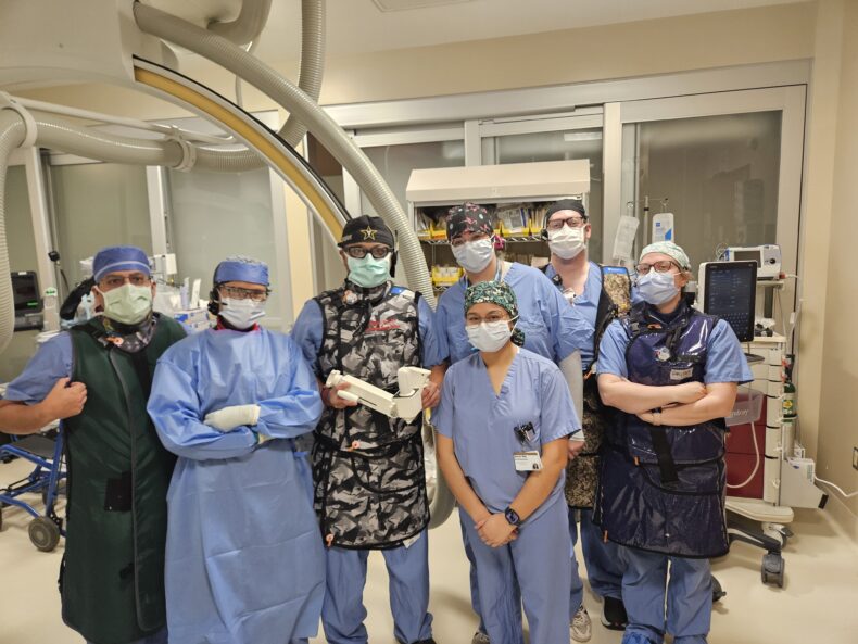 A group of doctors in blue scrubs and masks poses in the operating room