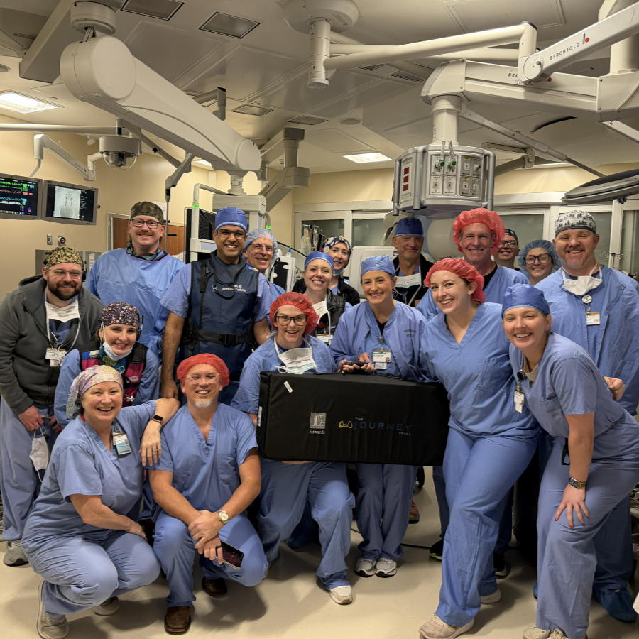 A dozen Cardiovascular Medicine J-Valve team members in blue scrubs pose in the operating room.
