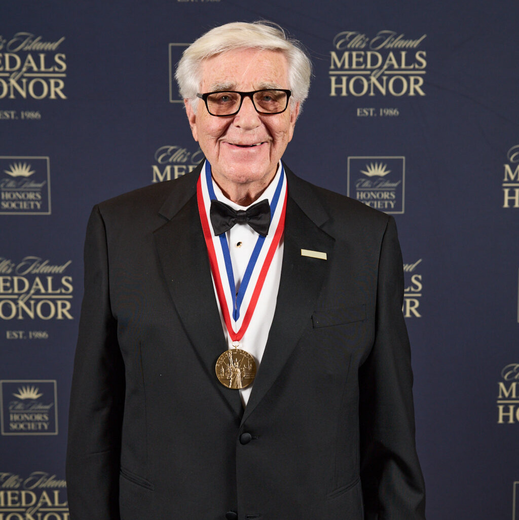 Dr. Billy Hudson, an older white male wearing a business suit and glasses, poses with his medal.