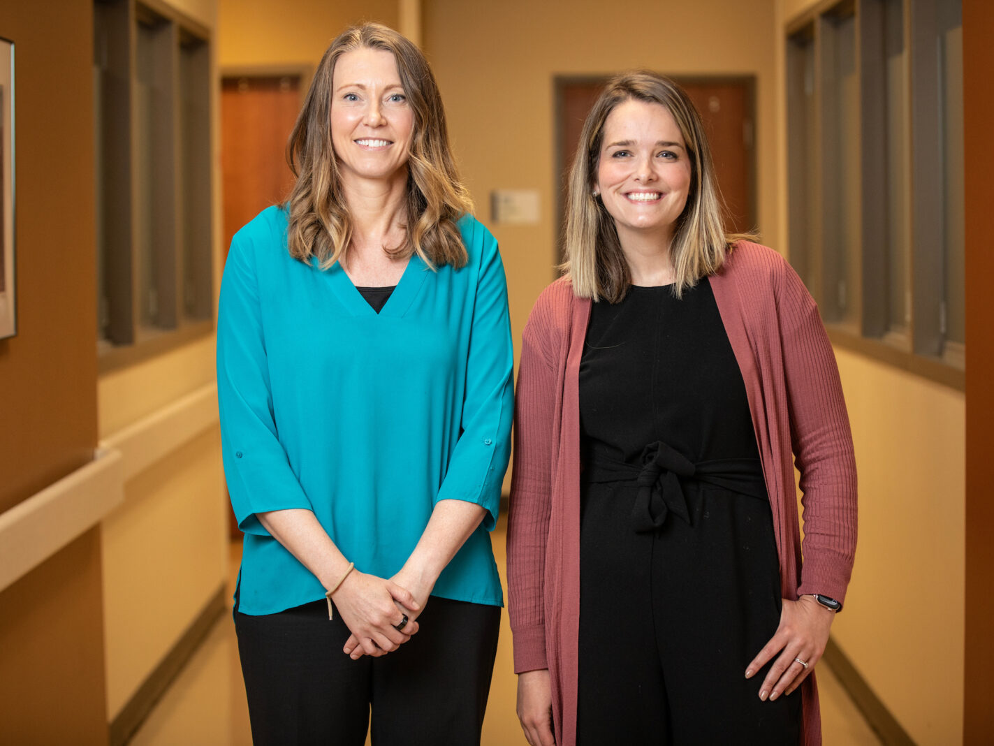 Drs. Missy Scalise and Kaylin Craig, two white female doctors in regular clothes, pose in a hospital hallway.