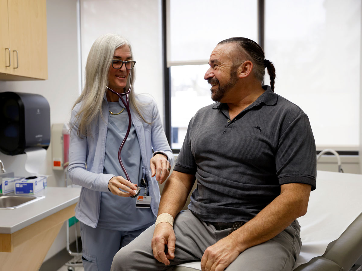 A female physician talks with a male patient in a clinic exam room.