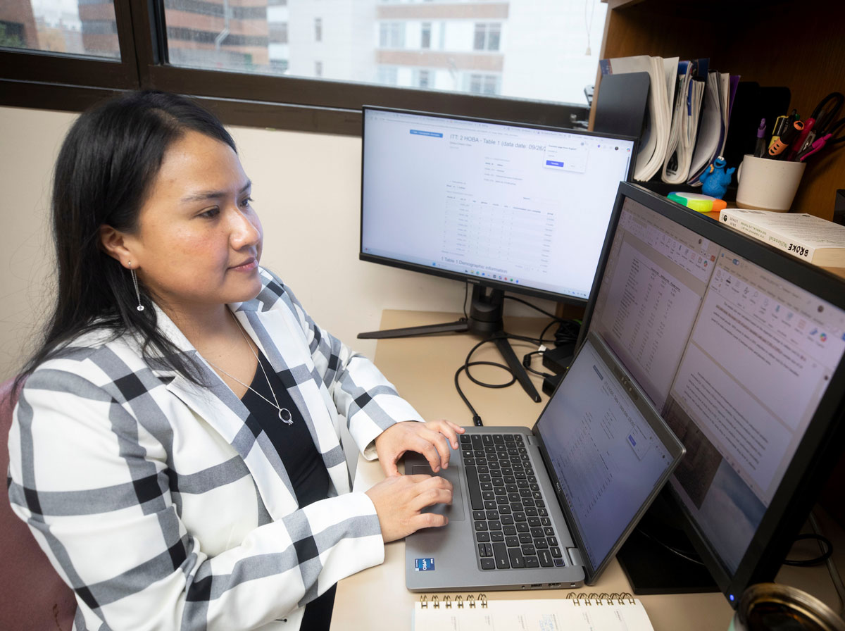 A young female researcher works in the lab using multiple computer screens.