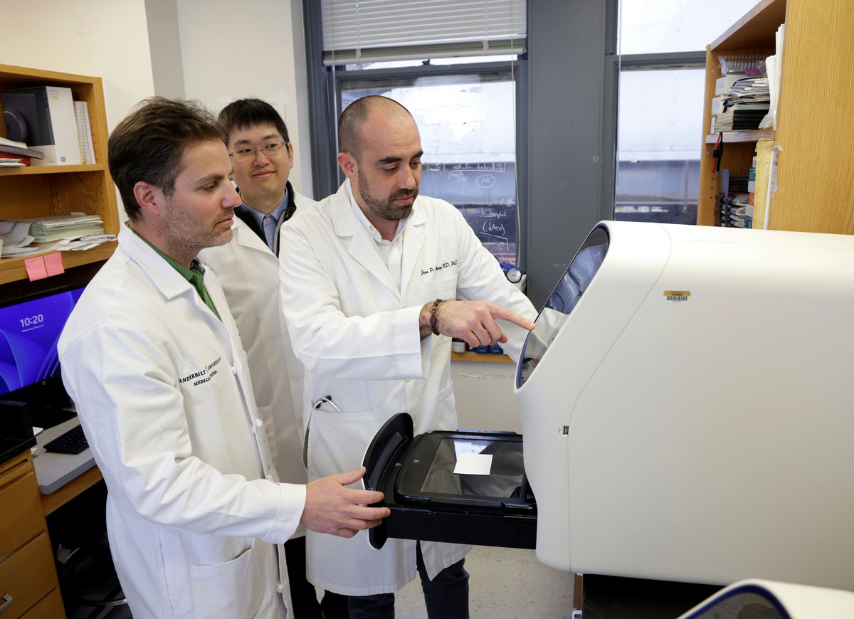 Three male researchers look at an instrument in the lab.