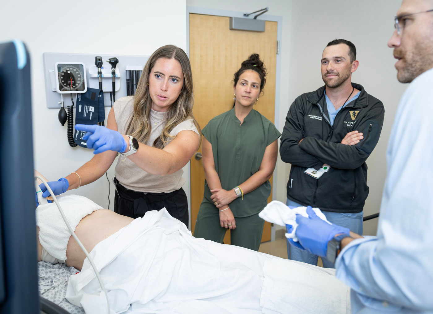 A nurse demonstrates an ultrasound on a patient volunteer while 4 other nurses look on.