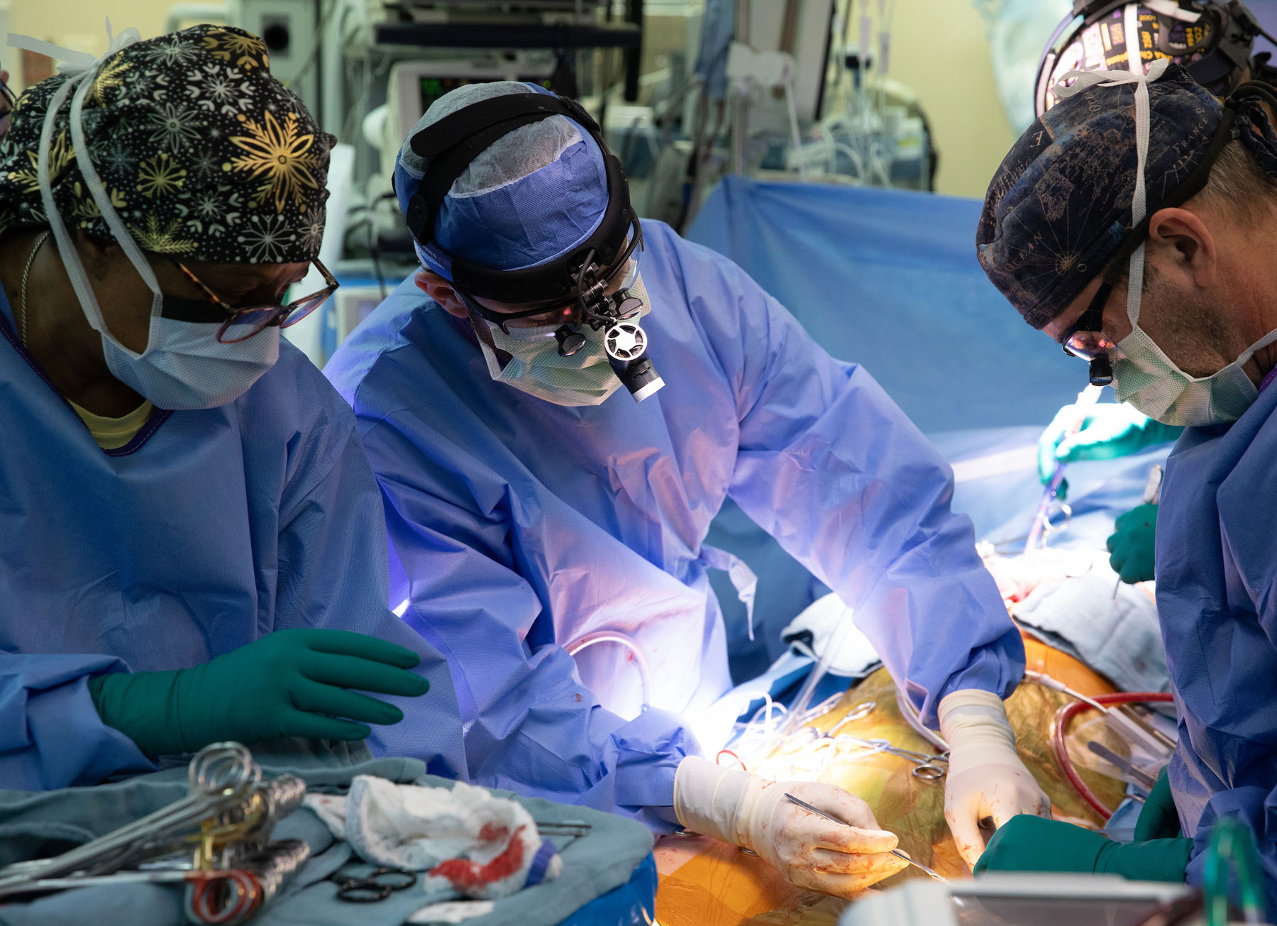 Three cardiac surgeons in full scrubs coverage operate on a patient.