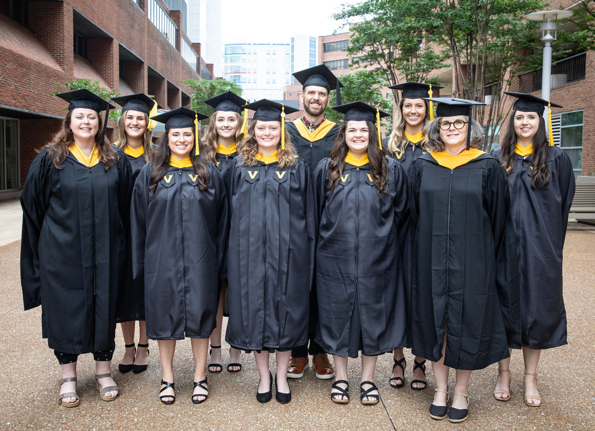 A group of 10 graduates in black caps and gowns poses outdoors at the medical center.