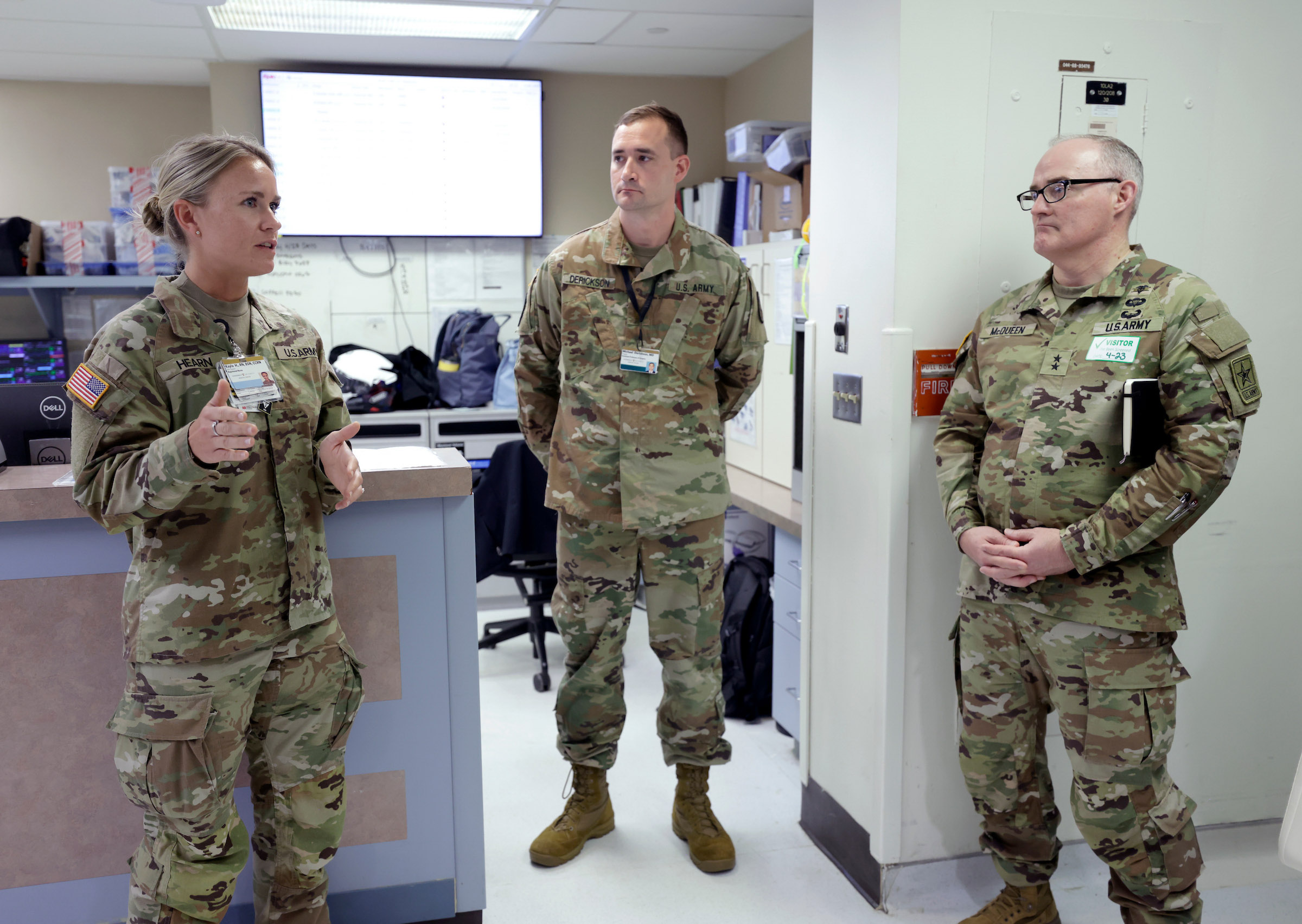 One female and two male Army service member talk at a hospital desk station.