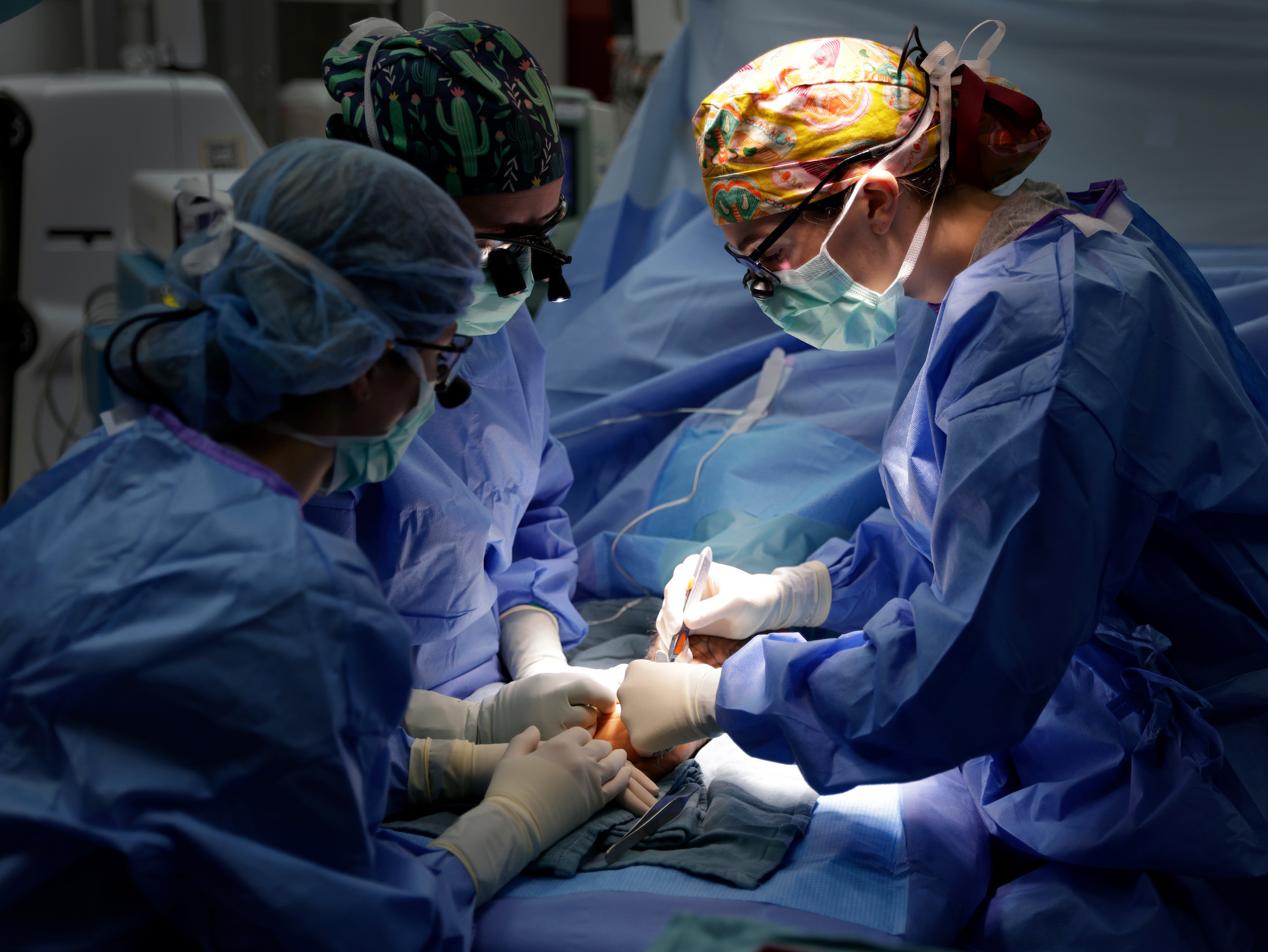 Three surgeons in full scrubs and low light conduct a liver transplant.