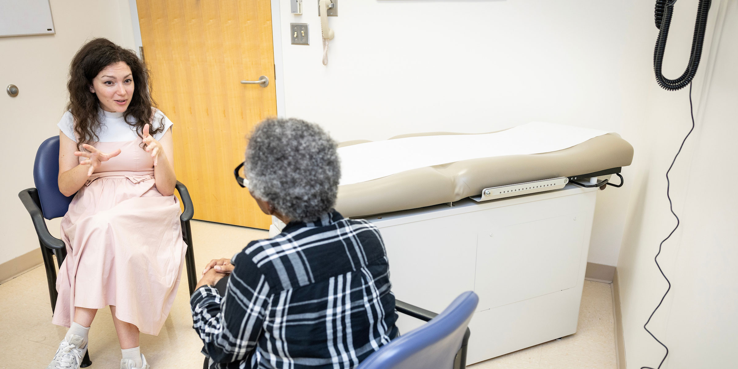 A young female physician speaks with a Black female patient in an exam room. 