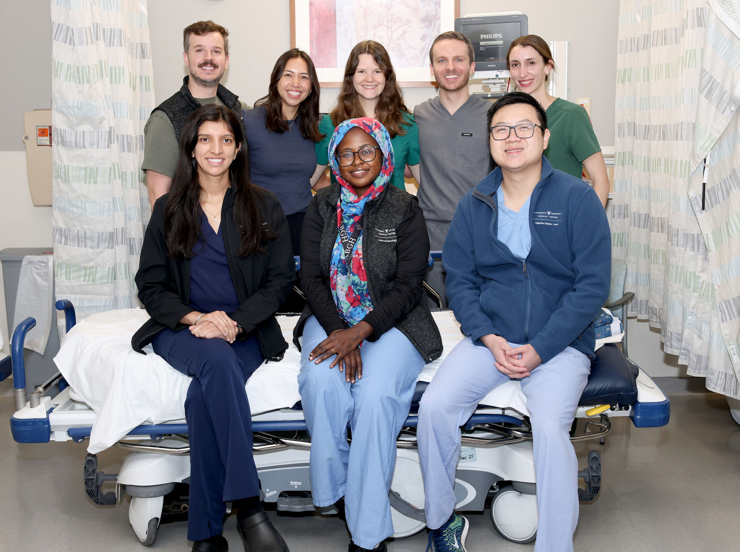 A group of eight GI fellows pose in a clinic exam room.