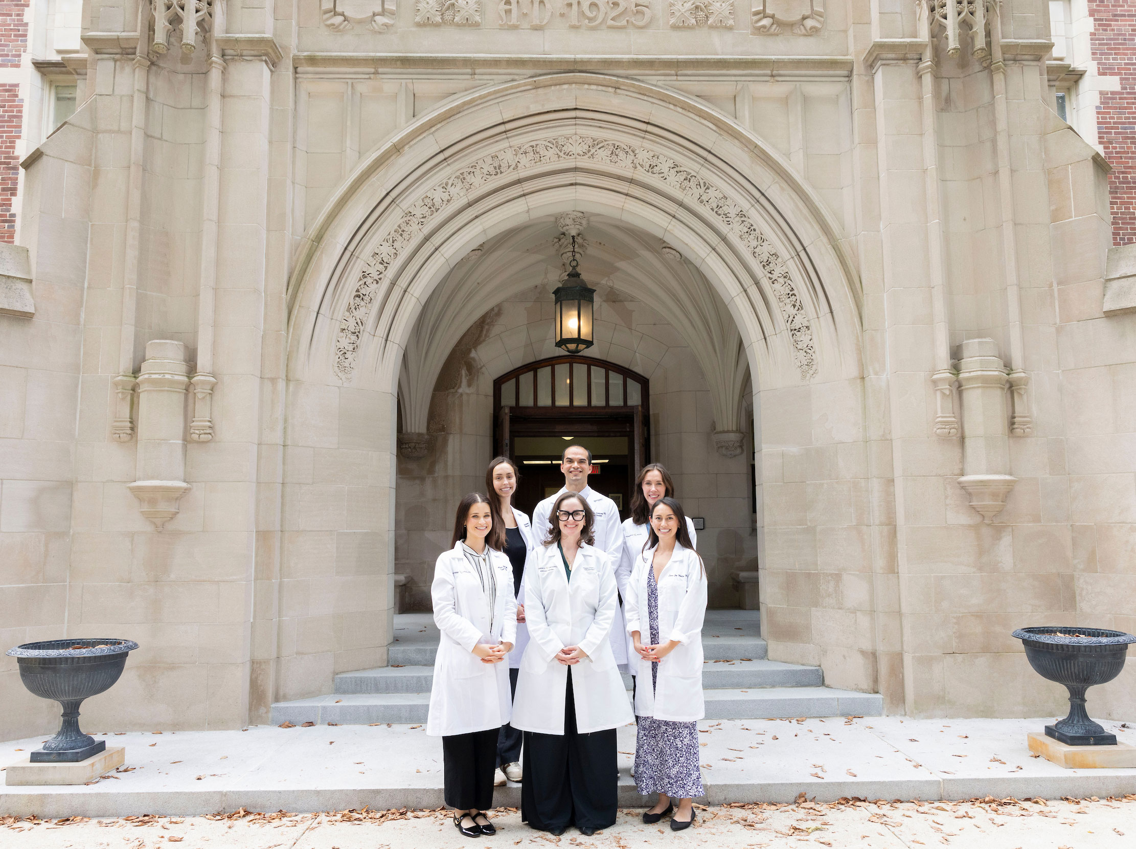 Five Internal Medicine chief residents in white lab coats pose with Dr. Megan Dupuis outside in Chapman Quad.
