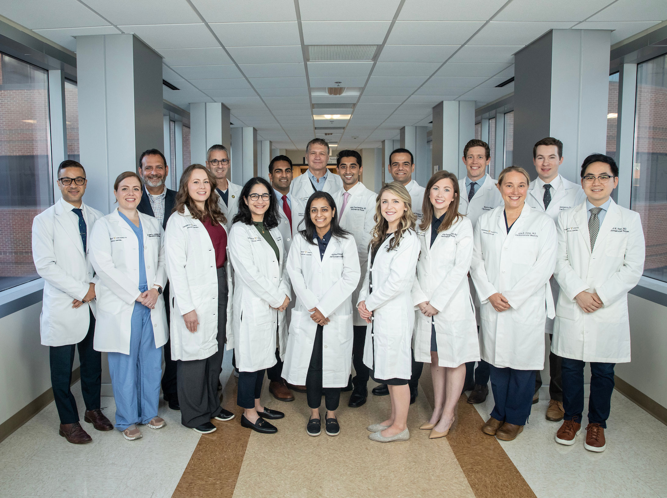 A group of 15 cardiology fellows and faculty mentors pose together on the sky bridge.