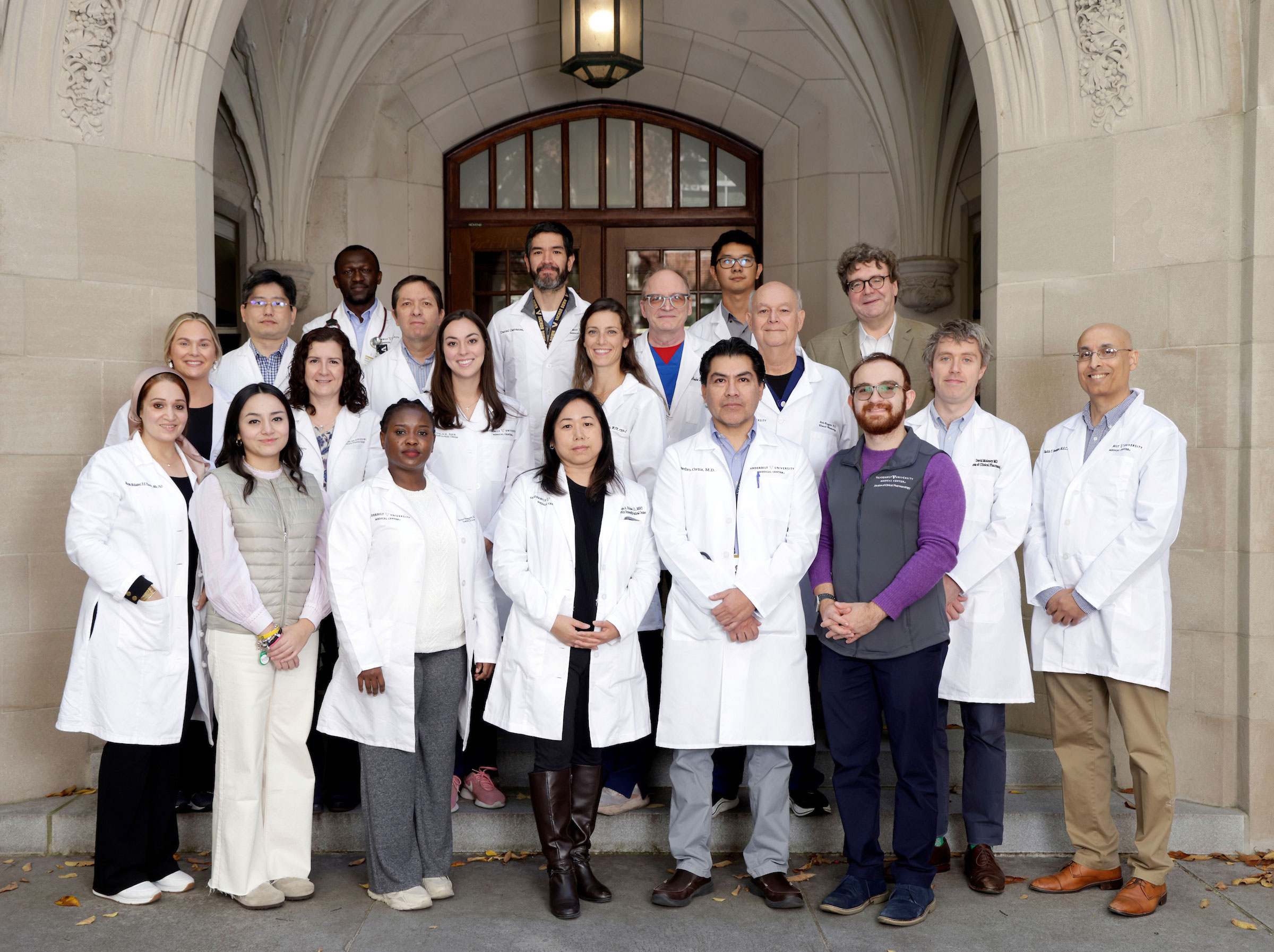 A group of about 20  medical personnel in white coats pose outside of an academic building.
