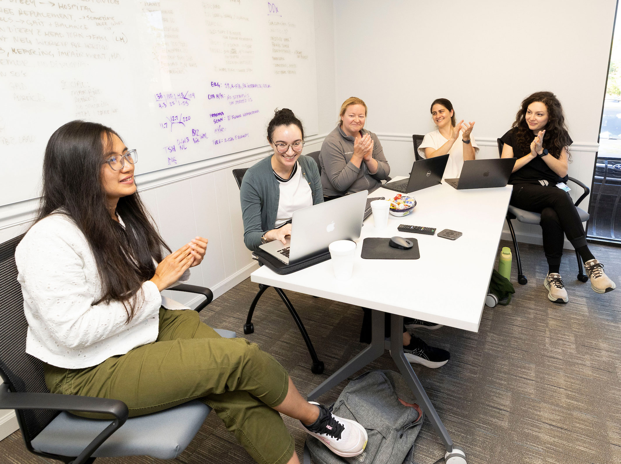 Five female physicians sit around a table in a small classroom.