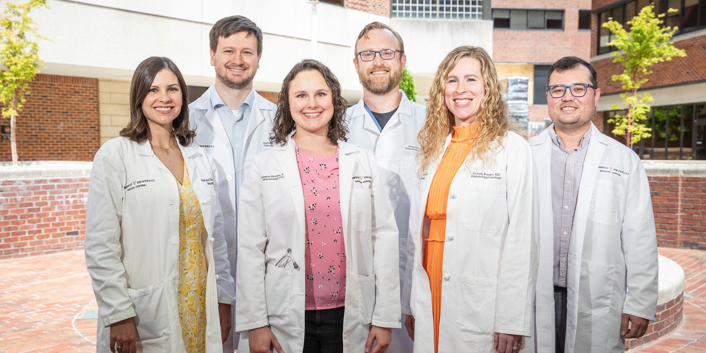 A group of six Hematology and Oncology fellows in white lab coats poses outside Vanderbilt hospital.