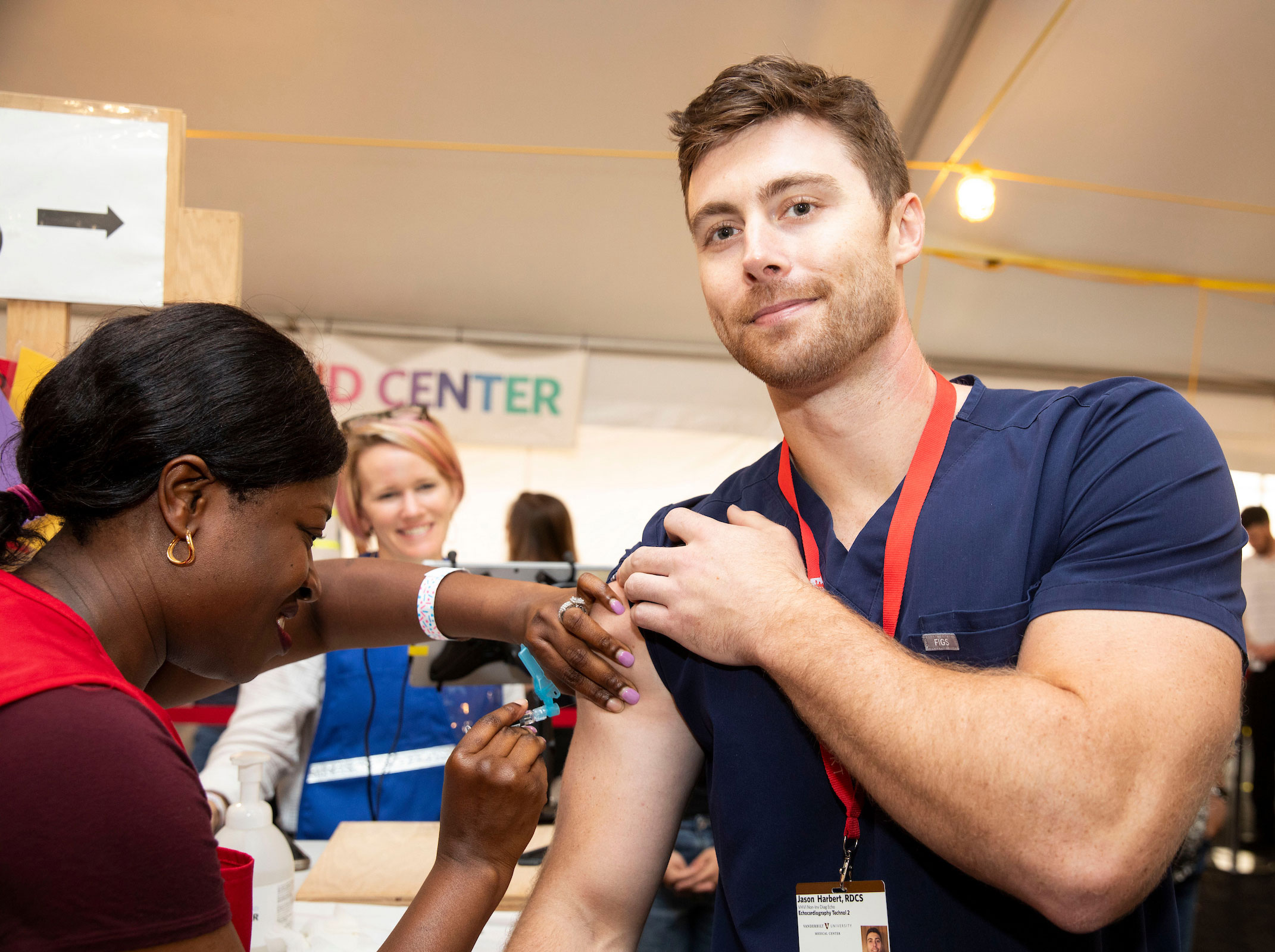 A young white man gets a flu vaccine from a Black health care provider.