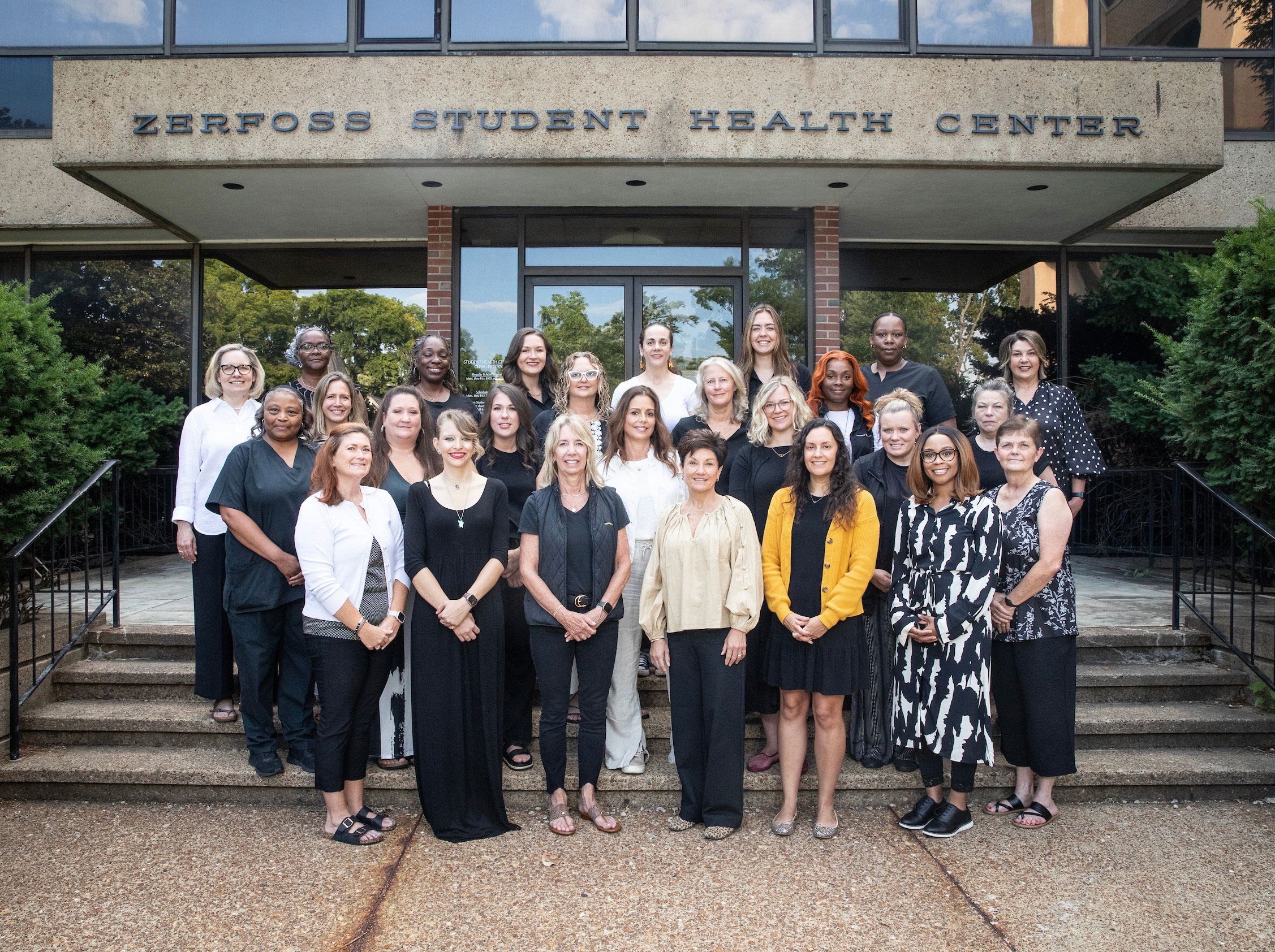 A large group of health care providers pose in front of the student health center.