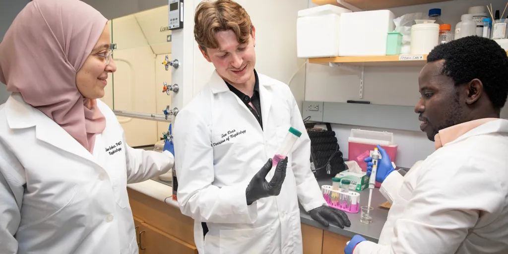 A female research scientist talks with two male lab members in her lab while looking at a test tube. 